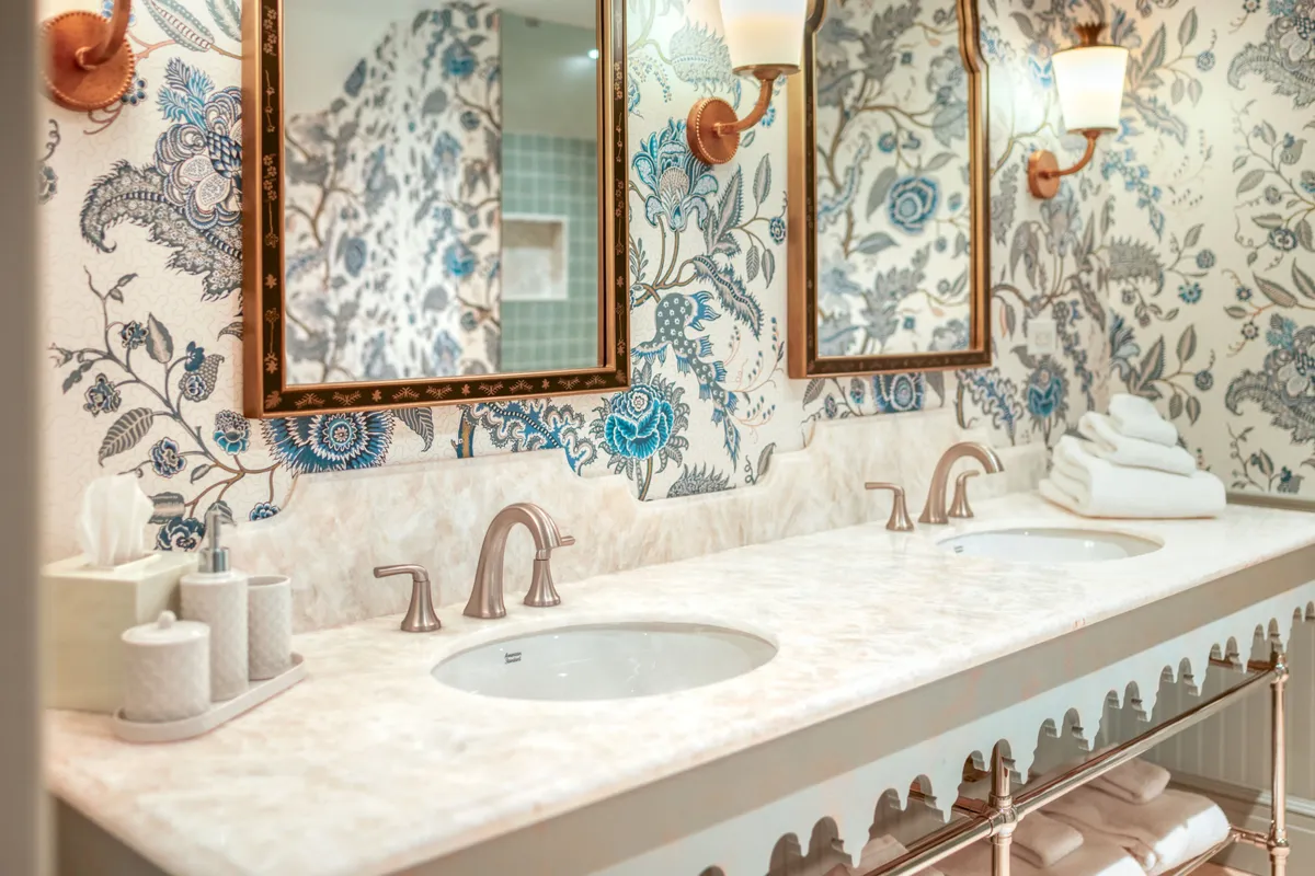 A sophisticated bathroom space with double sinks, ornate mirrors, and decorative wallpaper. The serene mood suggests a place for self-care and intimate daily routines, enhancing the suite’s sense of comfort and practical luxury.