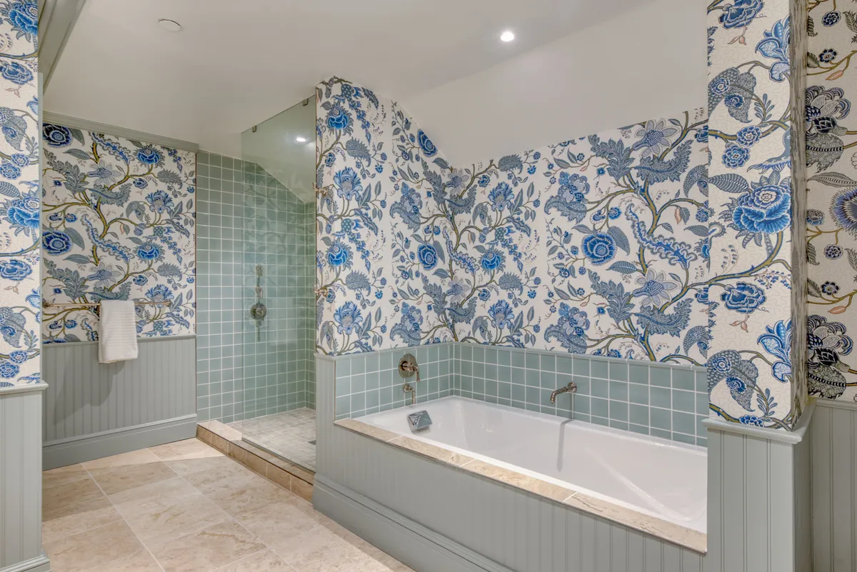 A calming bathroom featuring a deep soaking tub and a separate walk-in shower, set against decorative wallpaper. The inviting setup highlights an atmosphere of relaxation and rejuvenation, perfect for unwinding after a day by the shore.