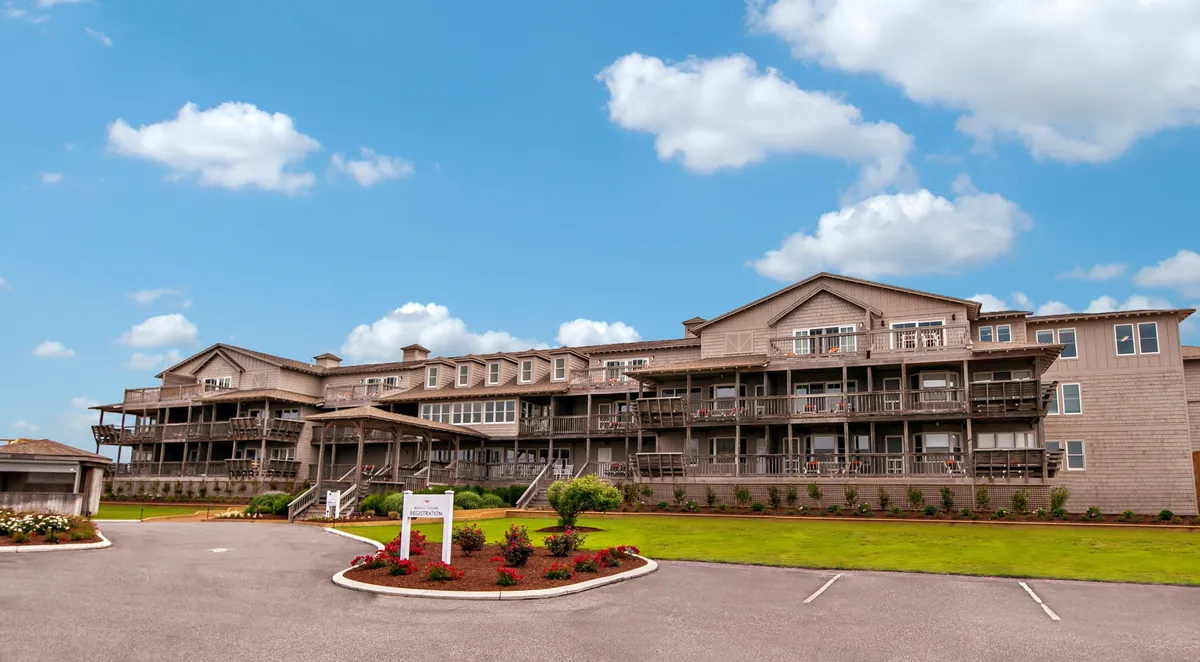 This image showcases the building's architecture with inviting balconies overlooking the surrounding landscaping and a bright blue sky. Some balconies are furnished, offering glimpses of outdoor relaxation spaces ideal for unwinding and taking in the view.